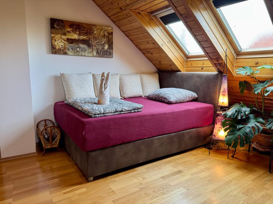 Ložnice s dvoulůžkem s vínovým přehozem pod střešními okny